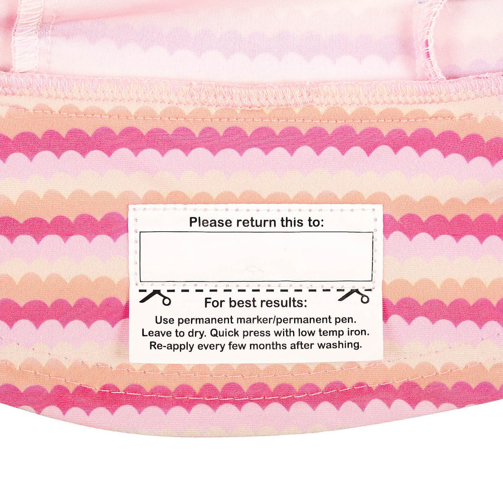Close-up of the name label on the inside brim of a swim bucket hat with a pink and peach scalloped stripe pattern.