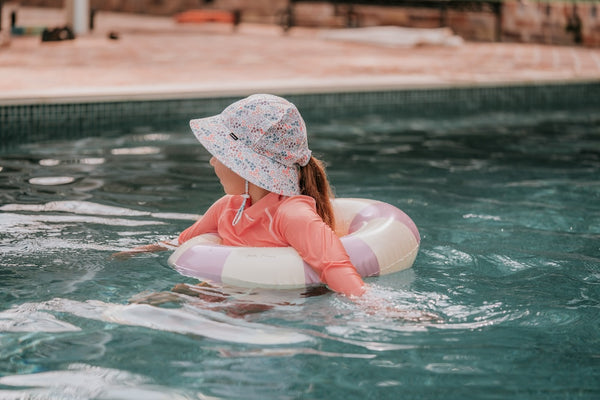 Side view of Bedhead Blossom Swim Bucket Hat worn by a young model using a floatation device and swimming in a swimming pool