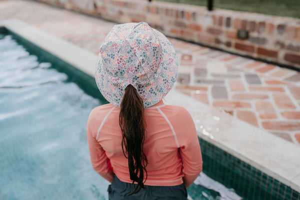 Back view of Bedhead Blossom Swim Bucket Hat worn by a young model with their ponytail through the back of the hat. Model is standing in a swimming pool.