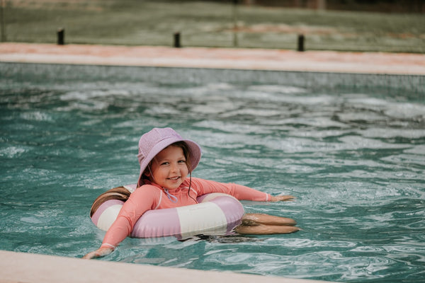 Bedhead Lila Swim Bucket Hat worn by a young model in a floatation ring in a swimming pool