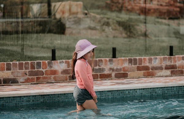 Bedhead Lila Swim Bucket Hat worn by a young model wading in a swimming pool