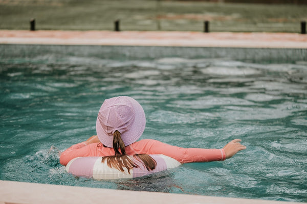 The back of Bedhead Lila Swim Bucket Hat worn by a young model using a floatation device in a swimming pool