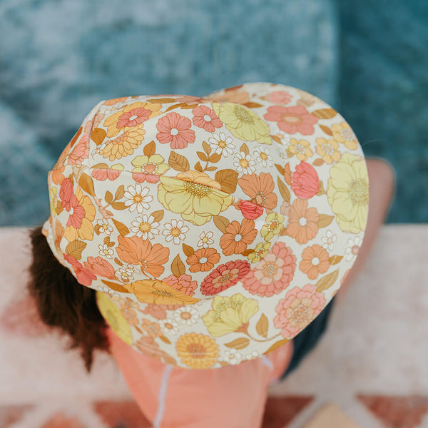 top view of Bedhead Tallulah Swim Bucket Hat worn by a young model sitting on the edge of a swimming pool