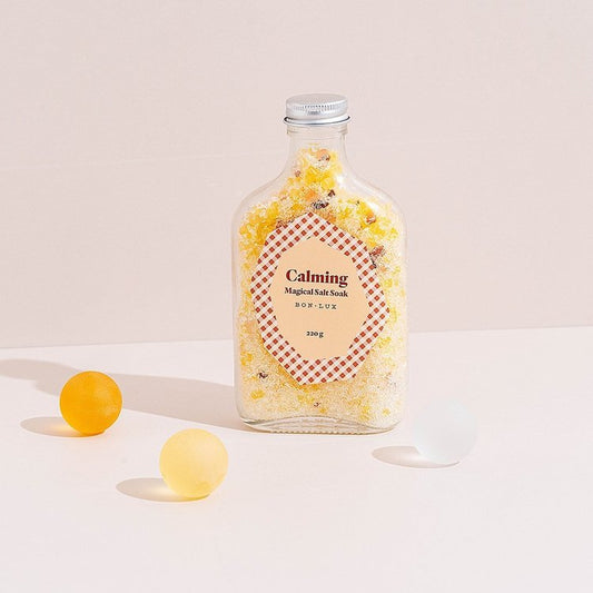 A bottle of Bon Lux Calming Magical Salt Soak with two yellow balls and a white ball on a light background.