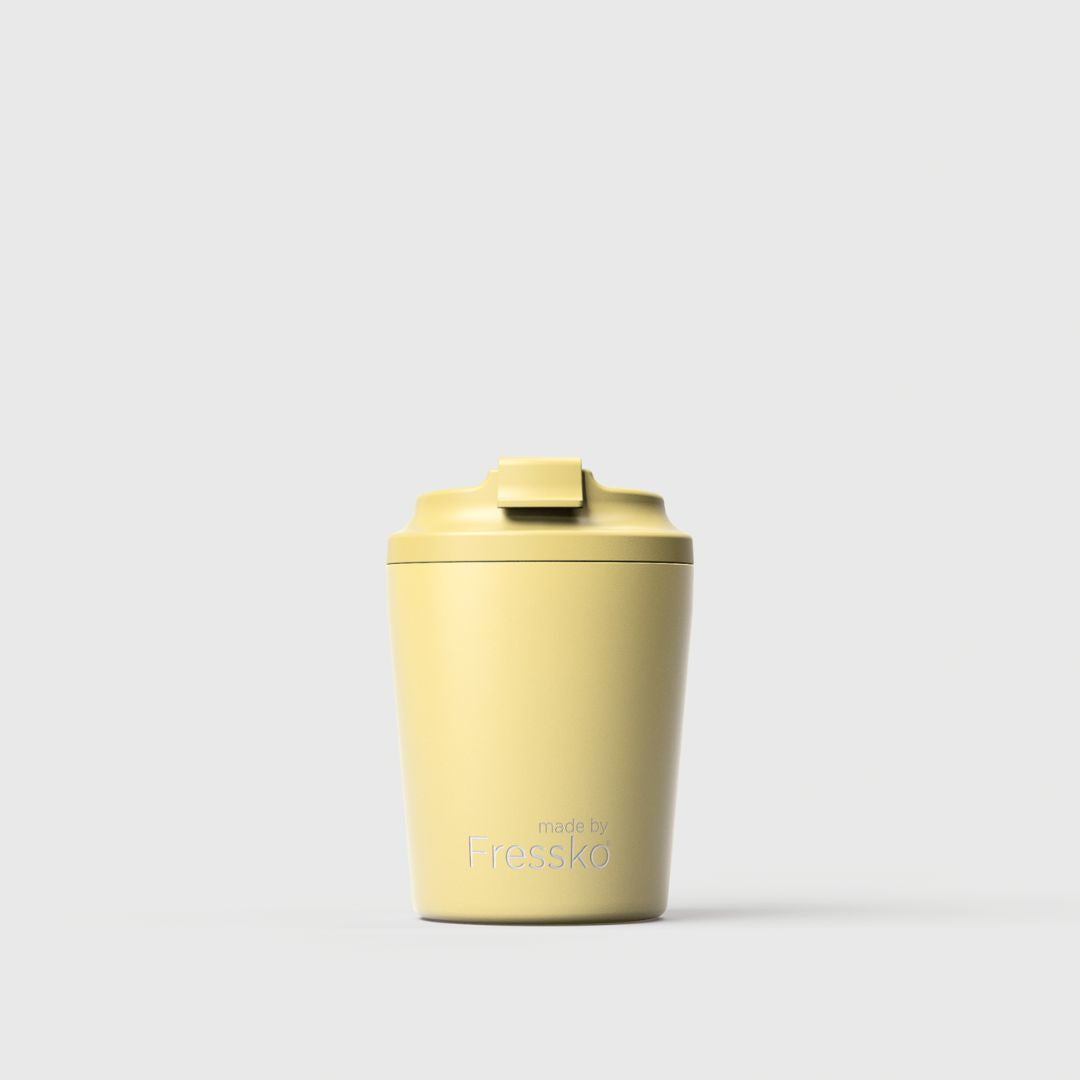 A pale yellow reusable travel tumbler with a matching flip-top lid, centered on a light gray background. The brand name 'Fressko' is printed near the bottom.