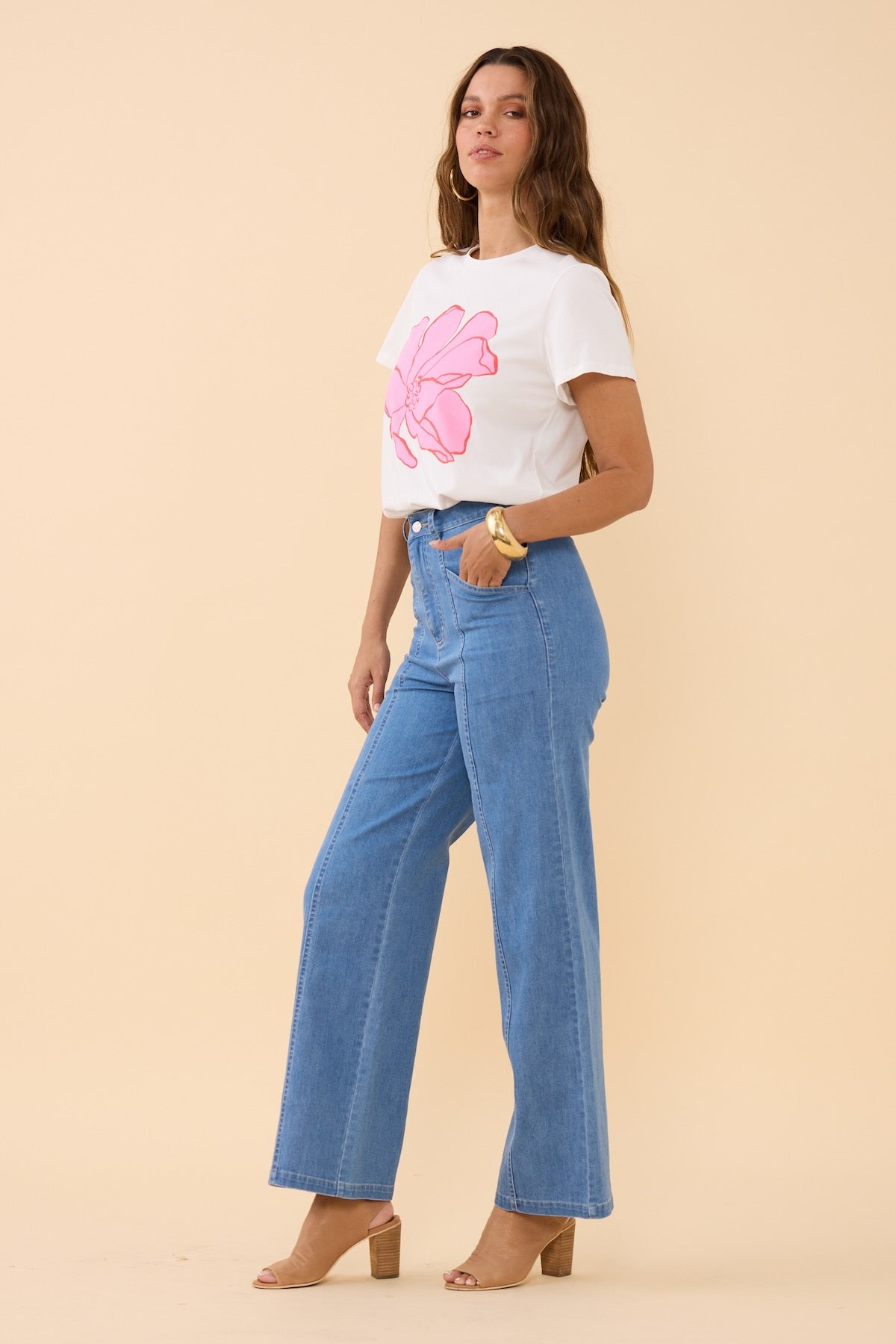 Woman wearing a white t-shirt with a pink floral design and blue jeans on a beige background