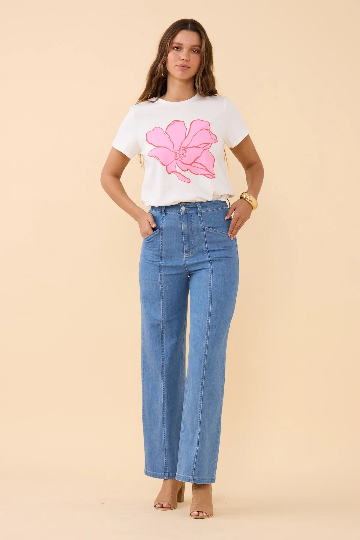 Woman wearing a white t-shirt with a pink floral design and blue jeans on a beige background