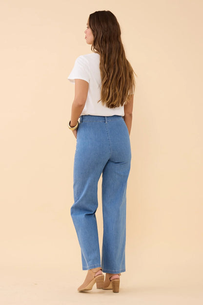 back view of woman wearing blue jeans and a white top on a beige background