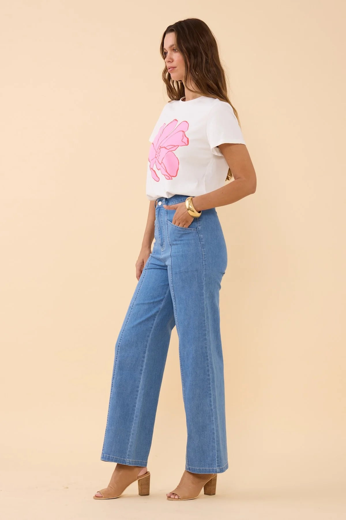 Side view of Woman wearing a white t-shirt with a pink floral design and blue jeans on a beige background