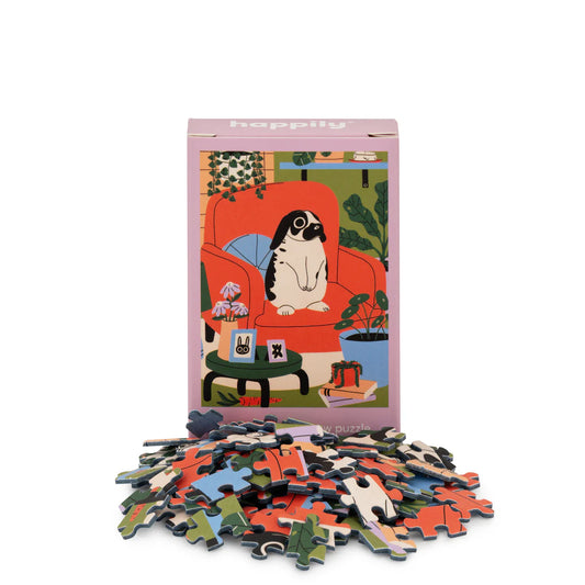 Puzzle box with colourful illustration of a lop-eared bunny sitting on an armchair, surrounded by scattered puzzle pieces on a white background.