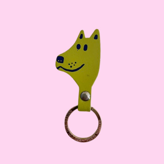 IMPERFECT lime green dog-shaped keychain with a silver metal snap button and a rose gold split key ring, shown against a solid pink background.