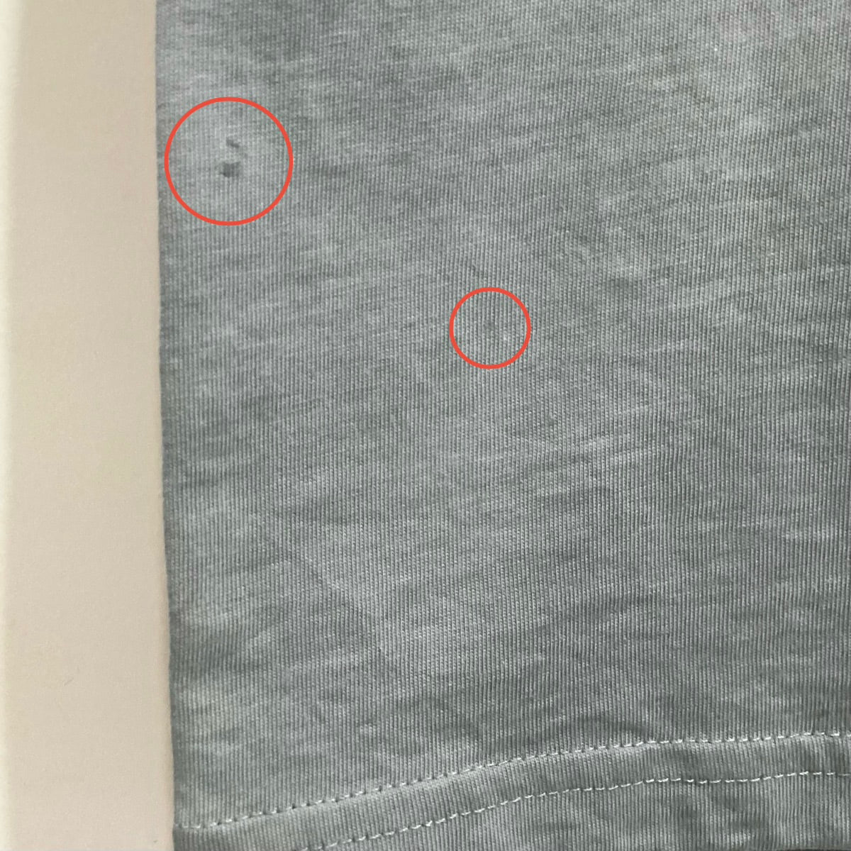 Closeup of blue-grey tee with two red circles highlighting imperfections