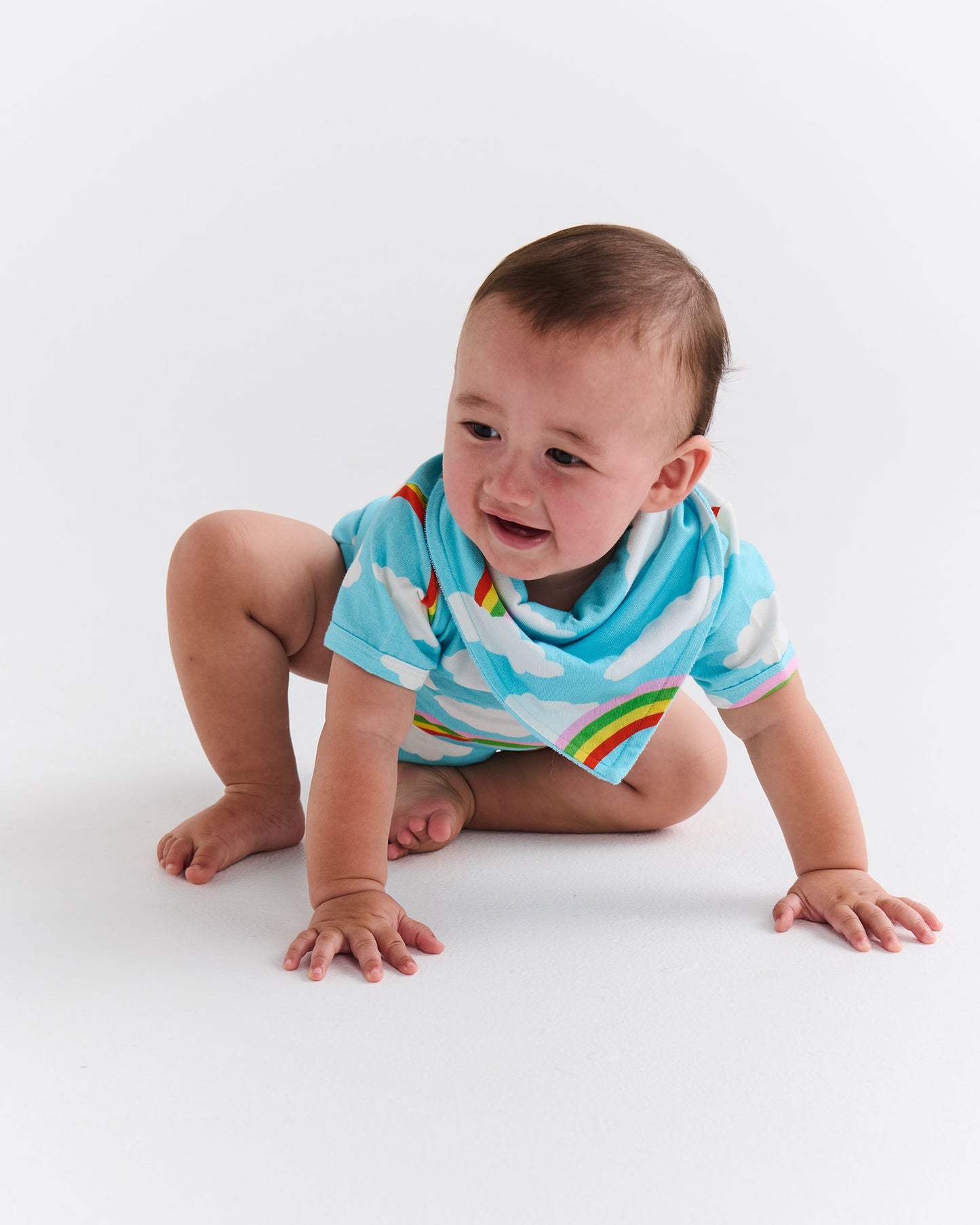 Baby wearing a blue striped onesie with the Cloudy Days design on a white background. The Cloudy Days design includes white clouds on a blue background, and rainbows.