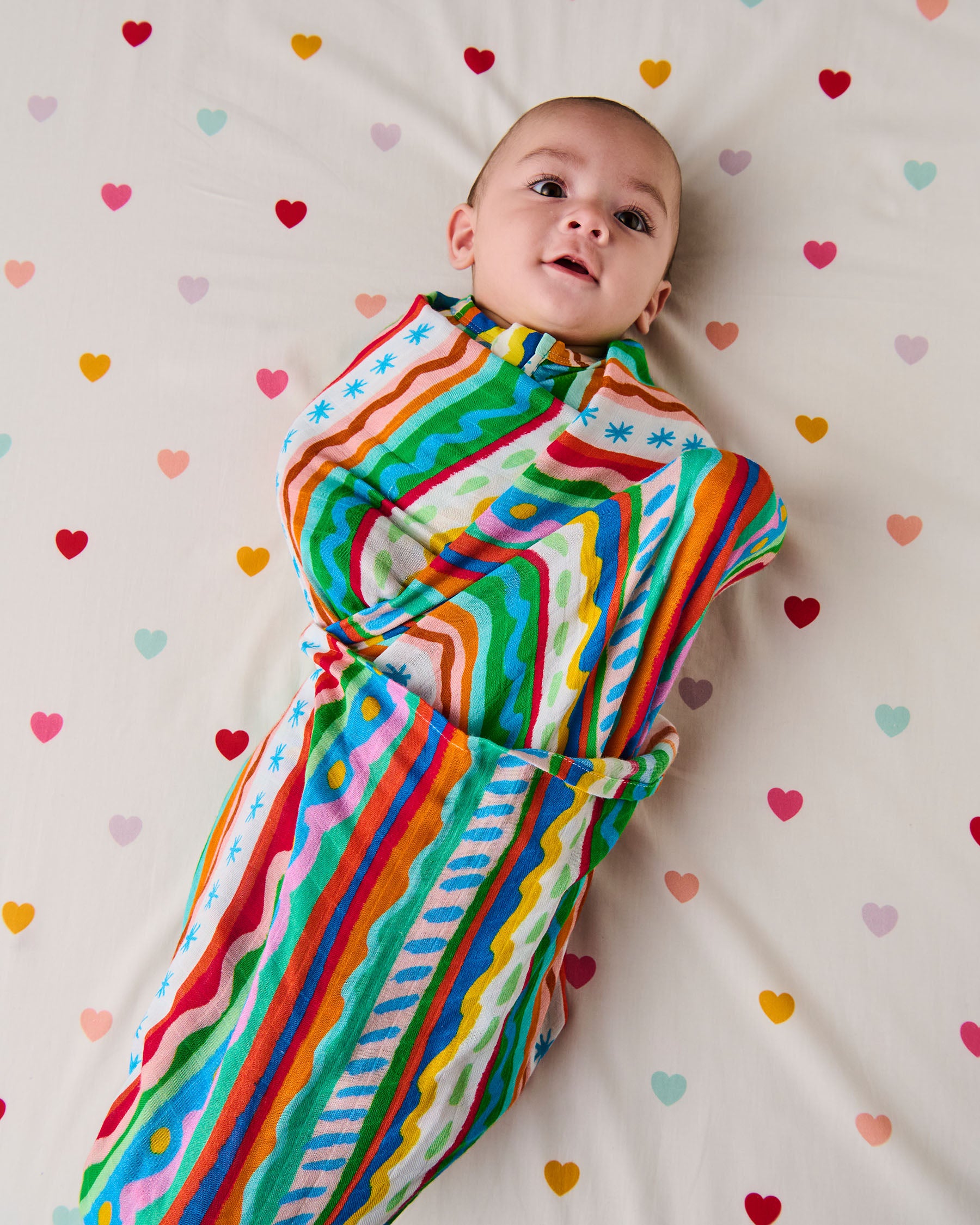 Baby wrapped in a colorful striped swaddle on a heart-patterned blanket