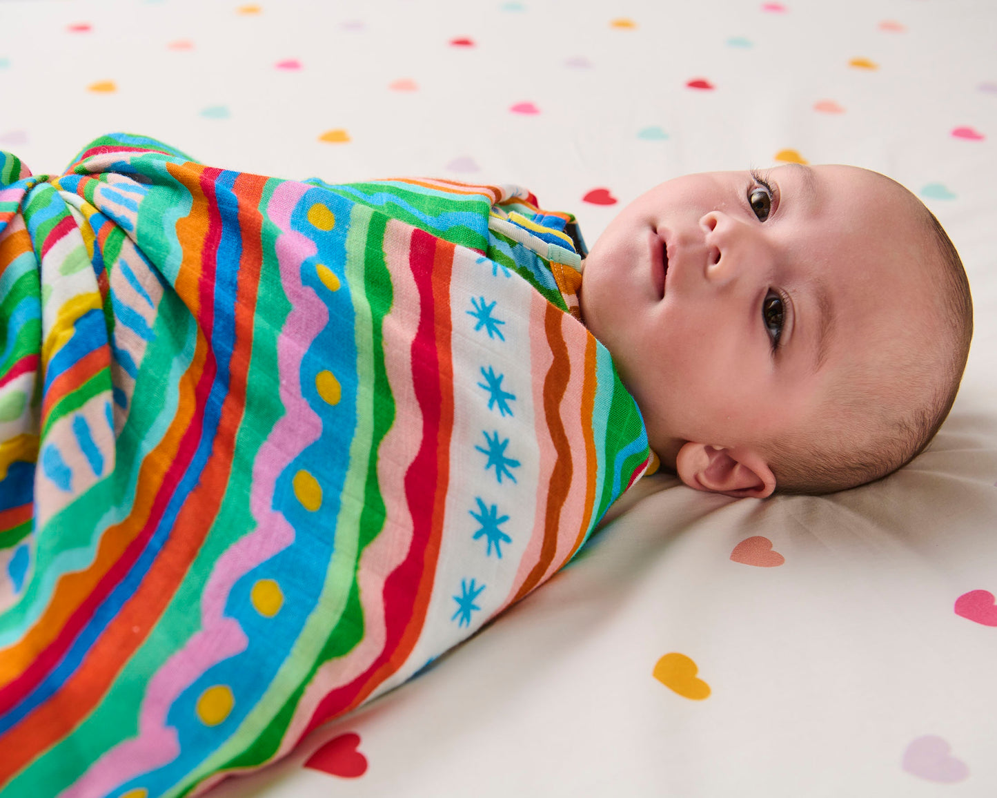 Baby wrapped in a colorful striped swaddle on a polka dot blanket