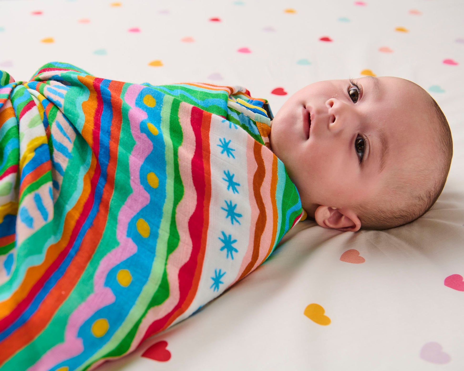 Baby wrapped in a colorful striped swaddle on a polka dot blanket