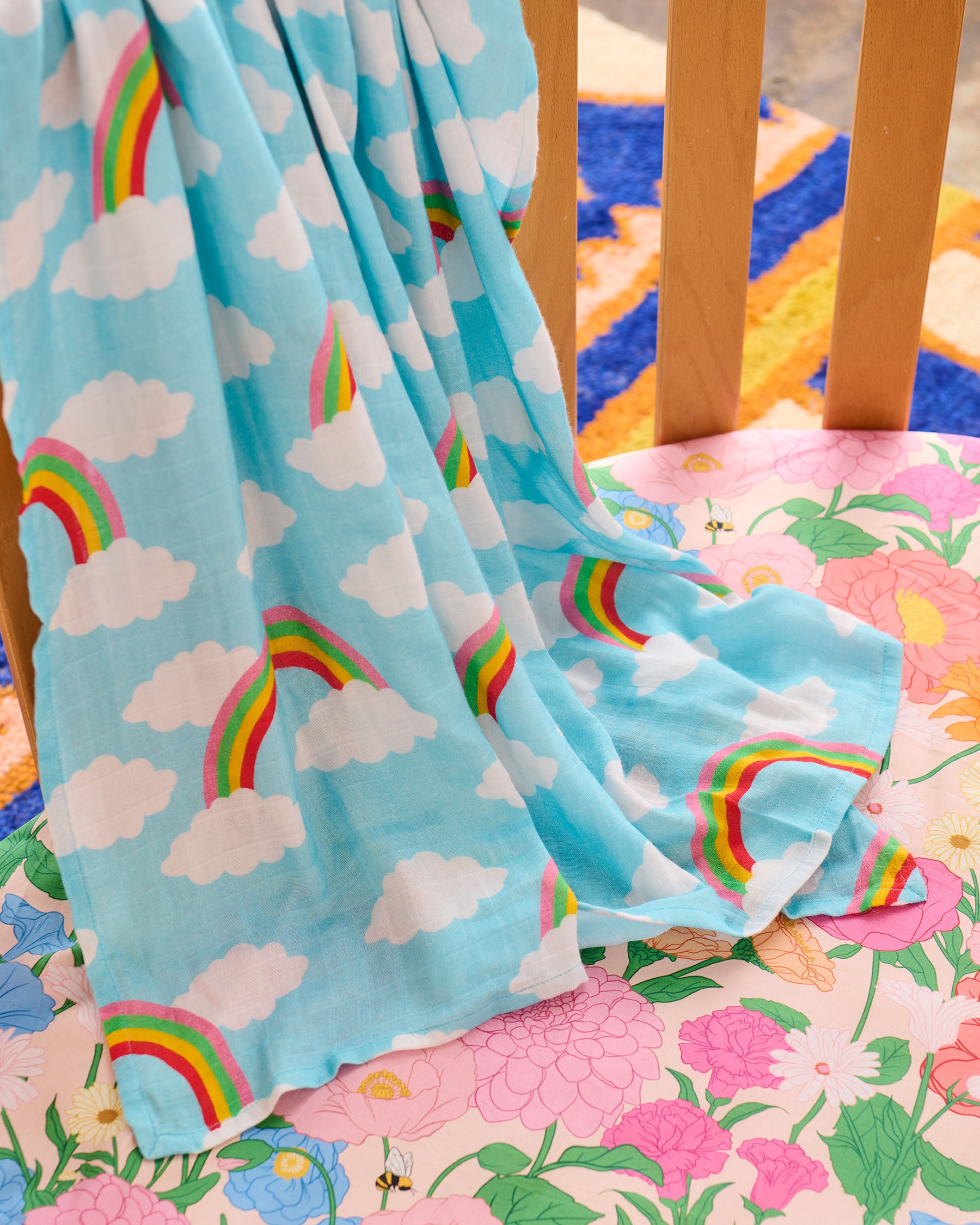 Children's blanket with rainbow and cloud pattern draped over a crib.