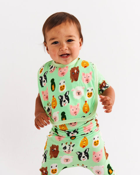 Styled image of a young toddler standing and wearing the Kip & Co Farm Friends Bib.