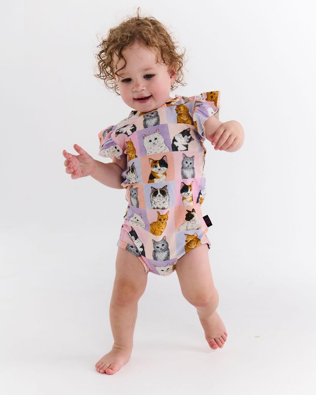 Baby wearing a colorful cat-patterned romper on a white background