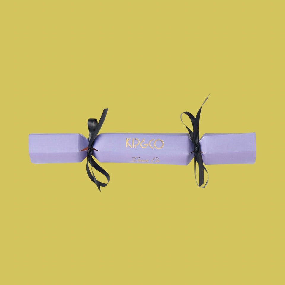 Packaging for Kip & Co Lilac Velvet Eye Mask - Purple cracker with black ribbons on a yellow background
