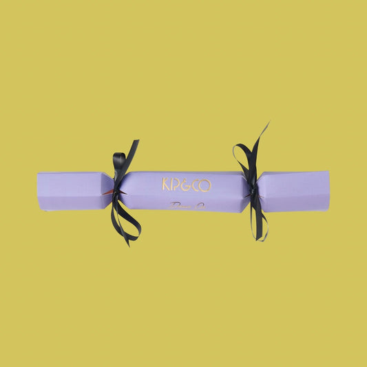 Packaging for Kip & Co Lilac Velvet Eye Mask - Purple cracker with black ribbons on a yellow background