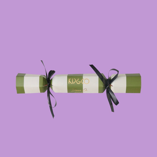 Packaging for Kip & Co Moss Stripe Velvet Eye Mask - Decorative cracker with green and white striped design and black ribbons on a purple background