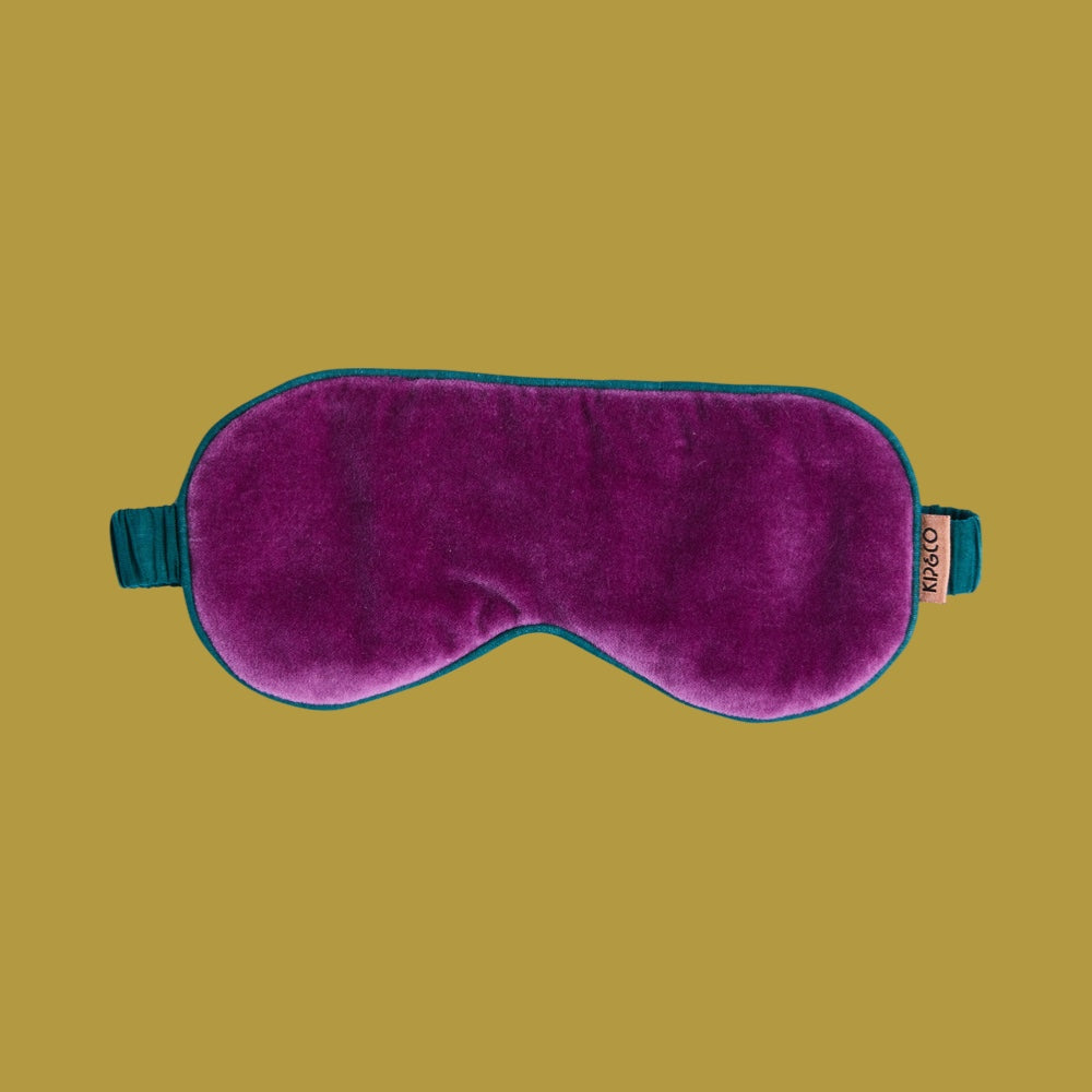 Purple sleep mask with teal straps on a beige background