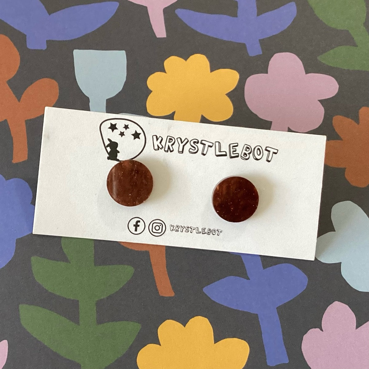 Brown round studs on a Krystlebot branded card against a colourful abstract background