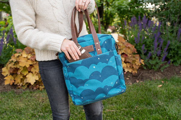 Close up of a model holding a Maika Commuter Tote in Plaka and they are pulling out a smaller pouch/ wallet from the front pocket of the tote.