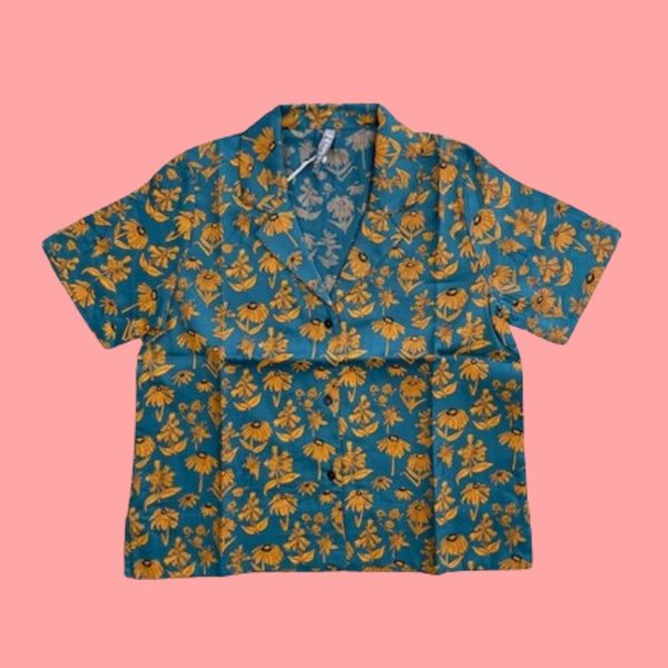 Mata Traders Camp Shirt in Teal Floral. This collared button-down shirt features a pattern of orange flowers and a teal coloured background.