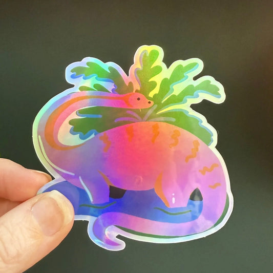 Holographic dinosaur sticker by Naomi Wilkinson, held by a hand against a dark background