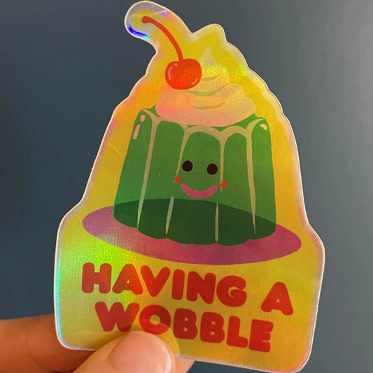 Holographic sticker by Naomi Wilkinson of a jelly with a cherry on top and 'Having a Wobble' text.