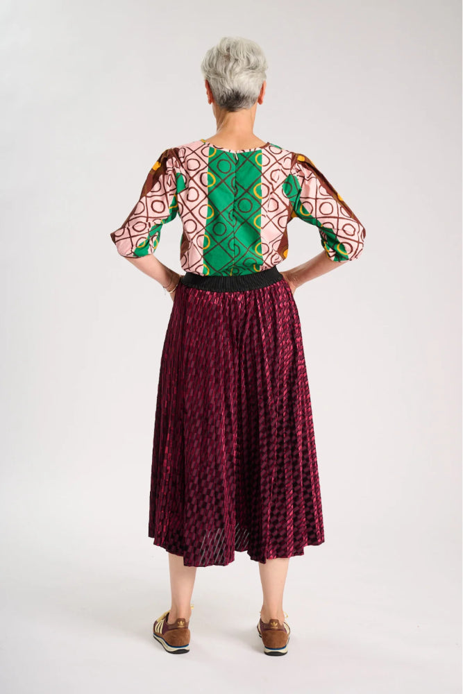 Back view of model wearing a colourful top and maroon skirt on a white background