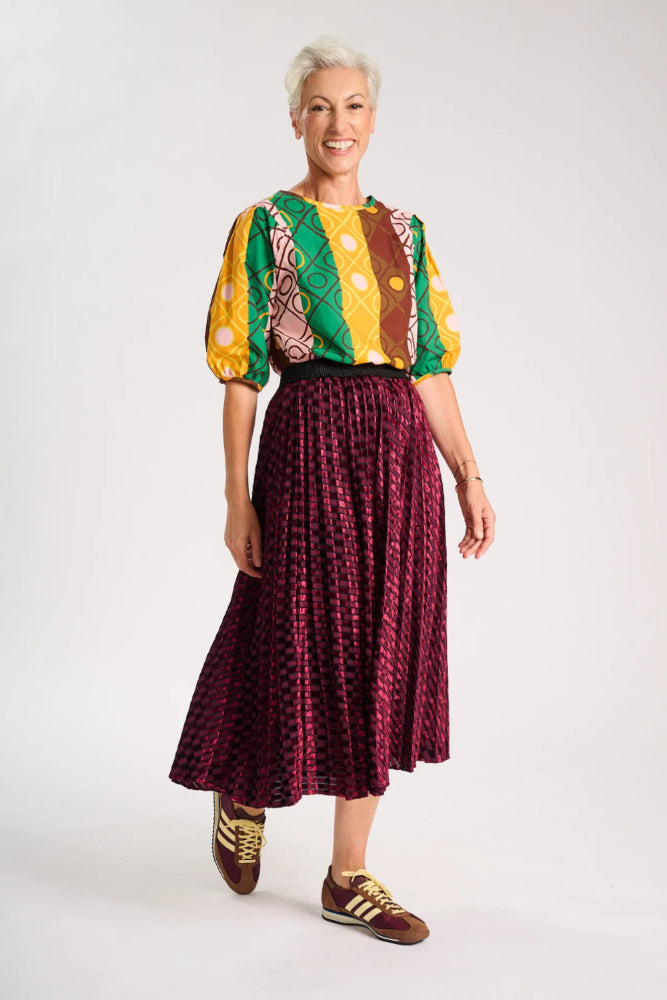 Model wearing a colourful top and maroon skirt on a white background