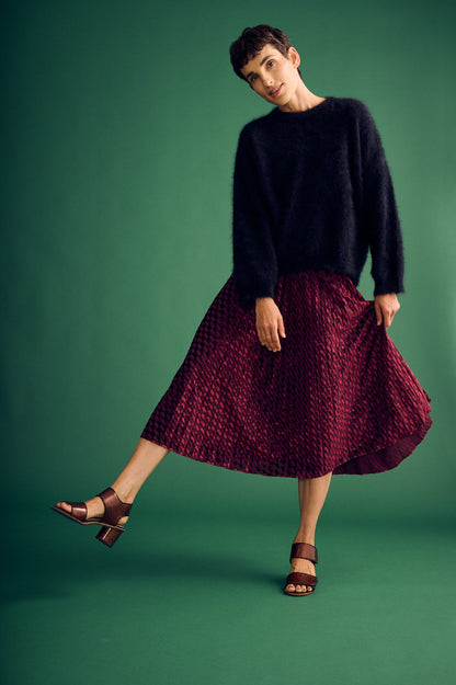 A woman wearing a black sweater and maroon-burgundy skirt on a green background