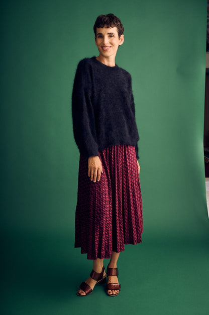 Woman wearing a dark sweater and red pleated skirt against a green background