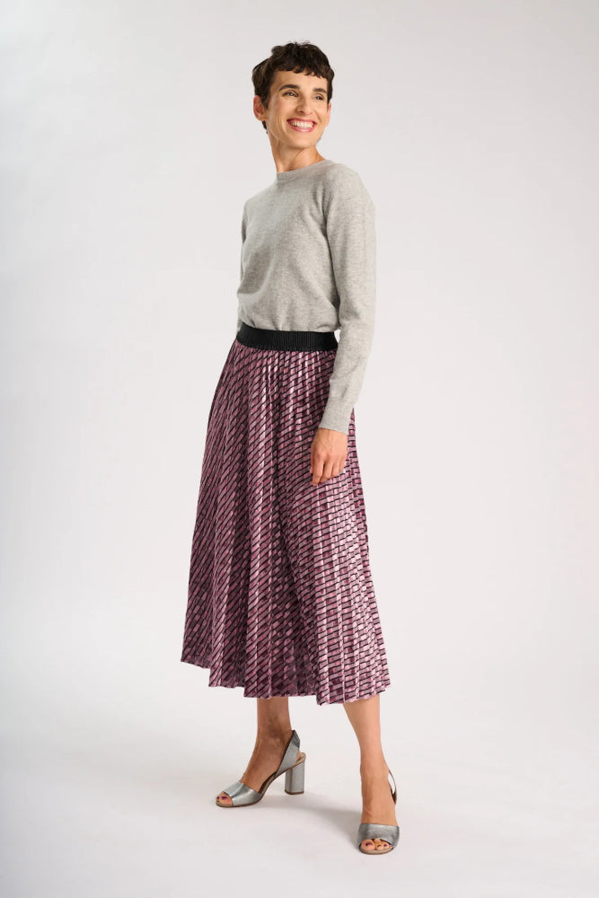 Side view of Model wearing a grey sweater and pale pink skirt on a white background