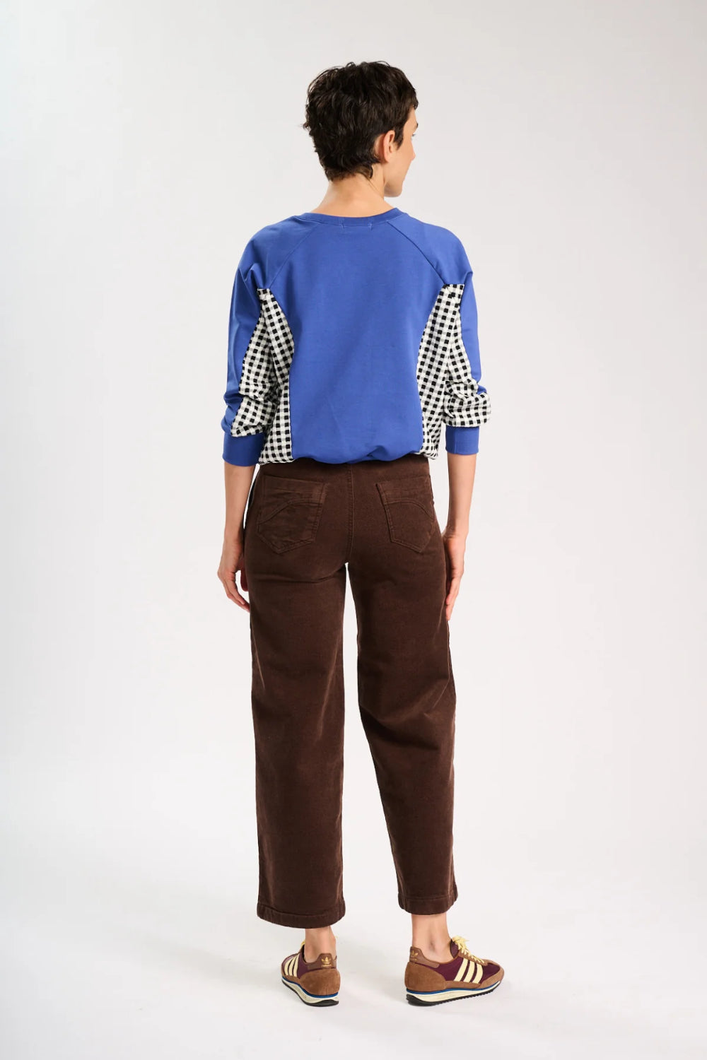 Back view of model standing and wearing a blue jumper and a pair of brown corduroy pants