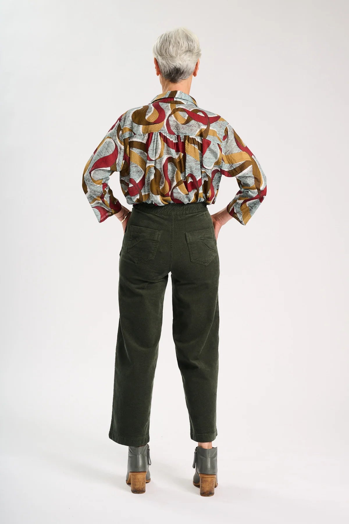 Back view of Model wearing Dark khaki green velvet pants with a colourful pattern shirt