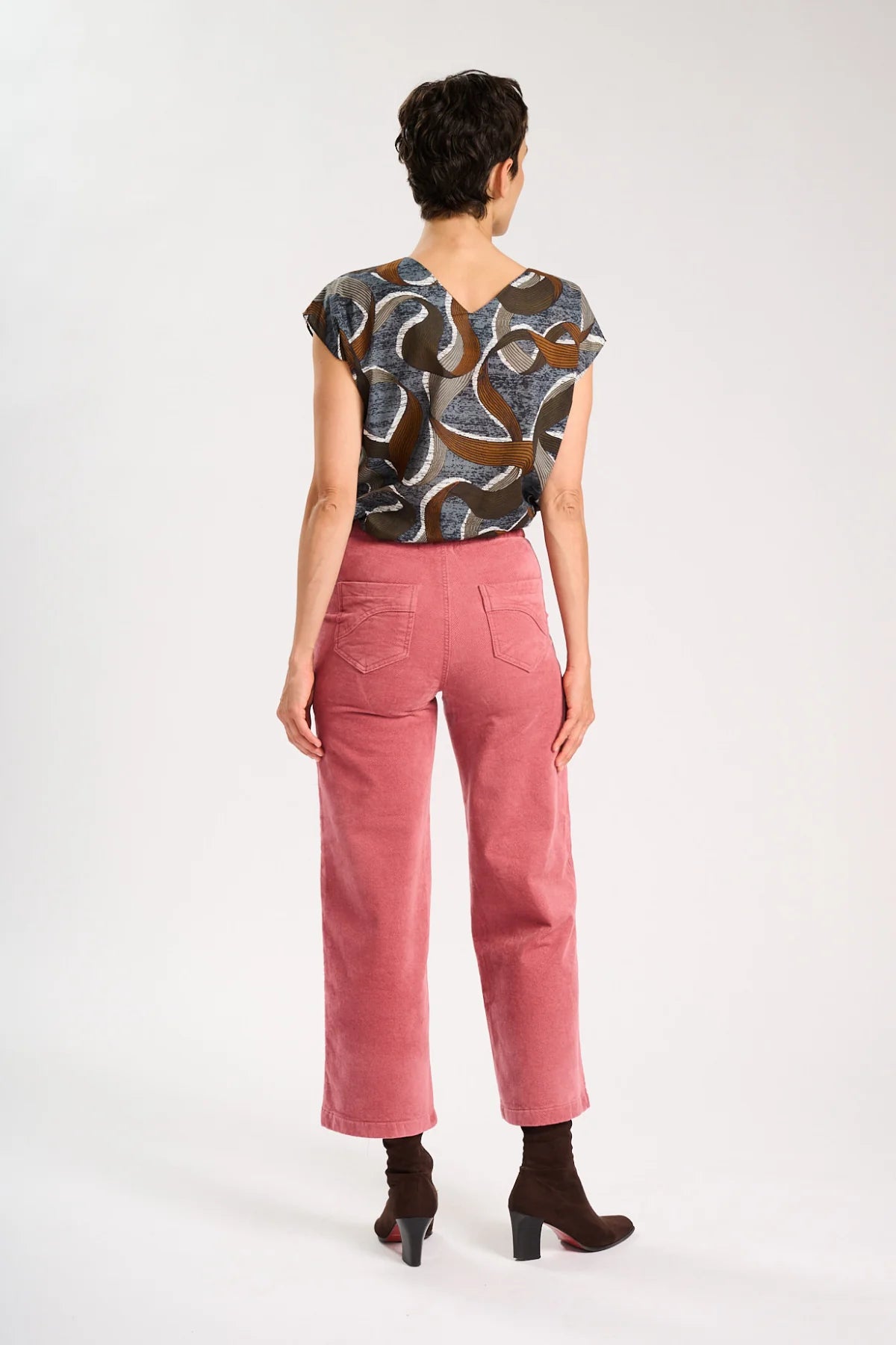 Back view of model wearing a brown patterned top and pink corduroy pants on a white background