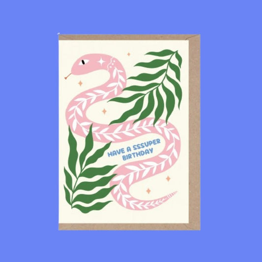 A birthday card with a pink snake and a couple leaves surrounding it. Text reading "Have A SSSuper Birthday". Kraft brown envelope. Solid pale blue background.