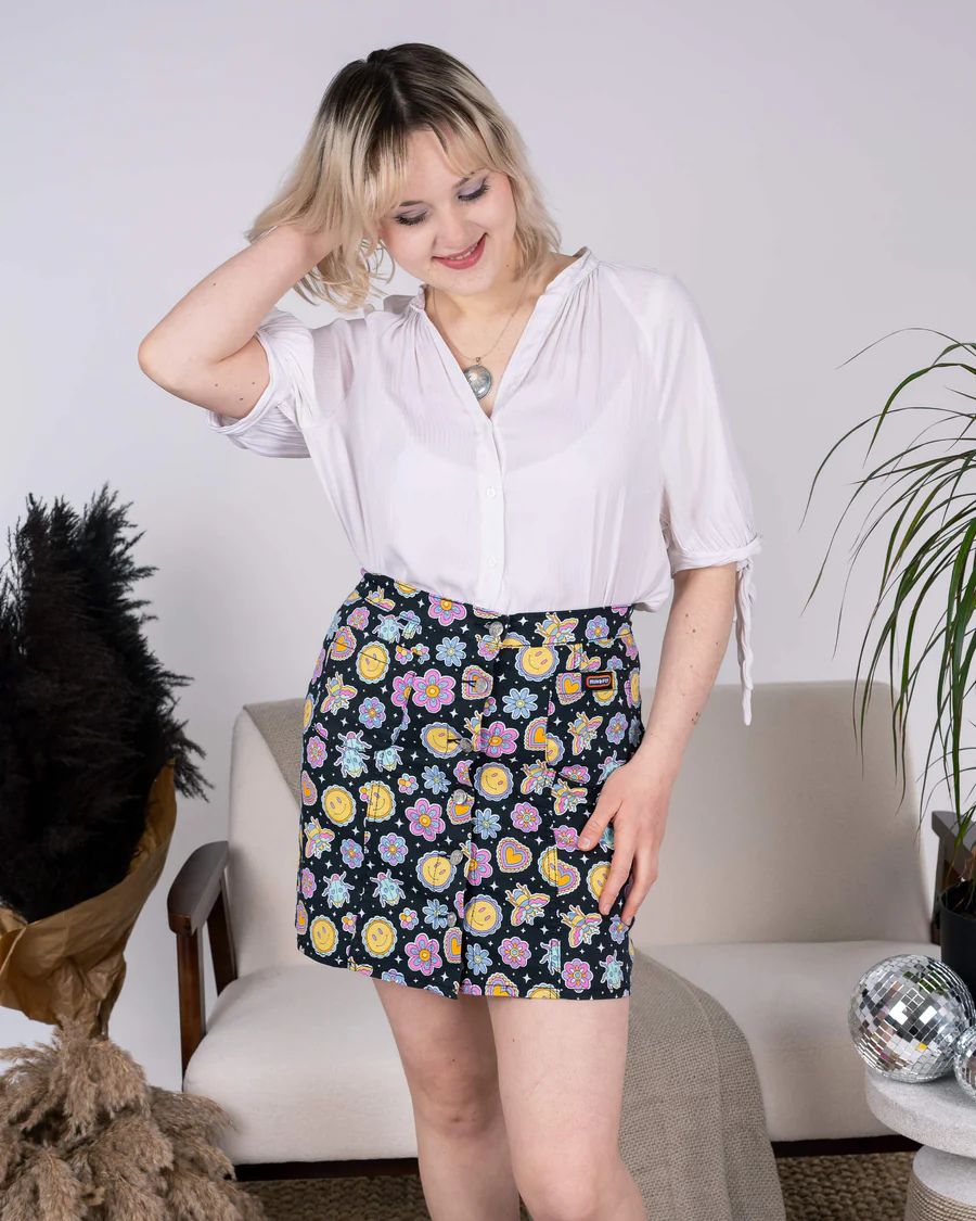 Model is wearing Run and Fly Bee Happy Mini Skirt. She is looking down toward the floor and smiling.