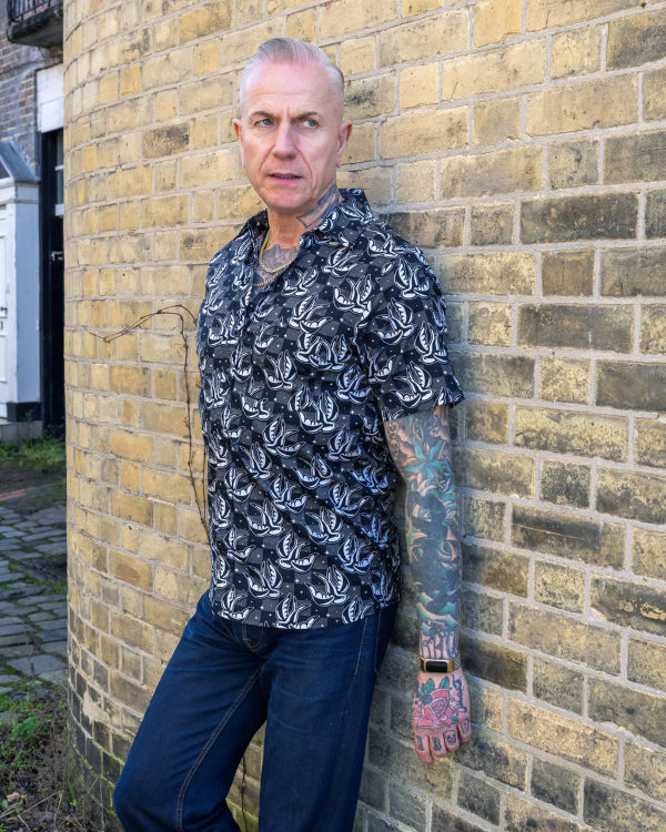 Model is wearing Run and Fly Swallows Checkerboard Shirt and posing in front of a brick wall, looking away from the camera.